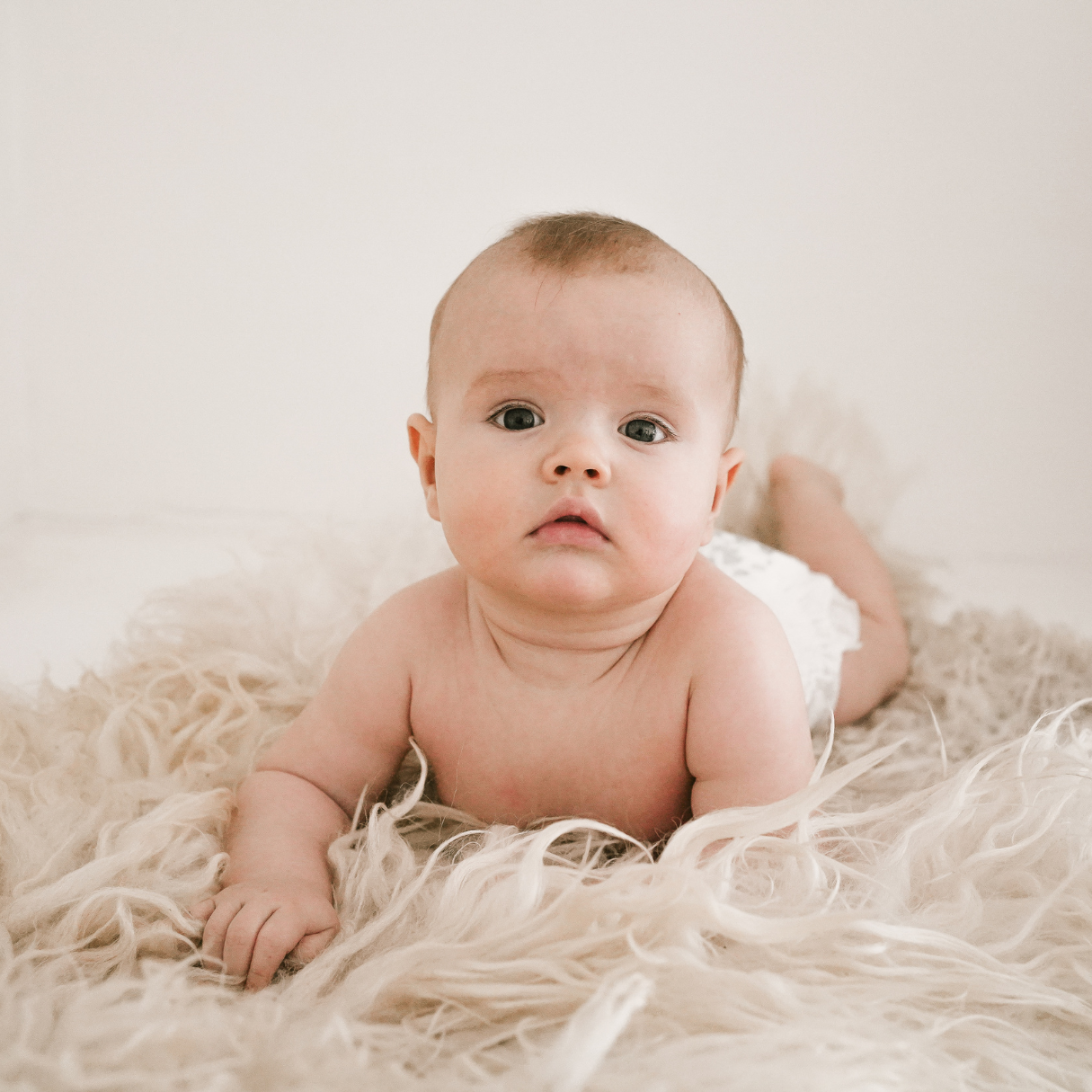 Baby lying on a fluffy white surface with a neutral background