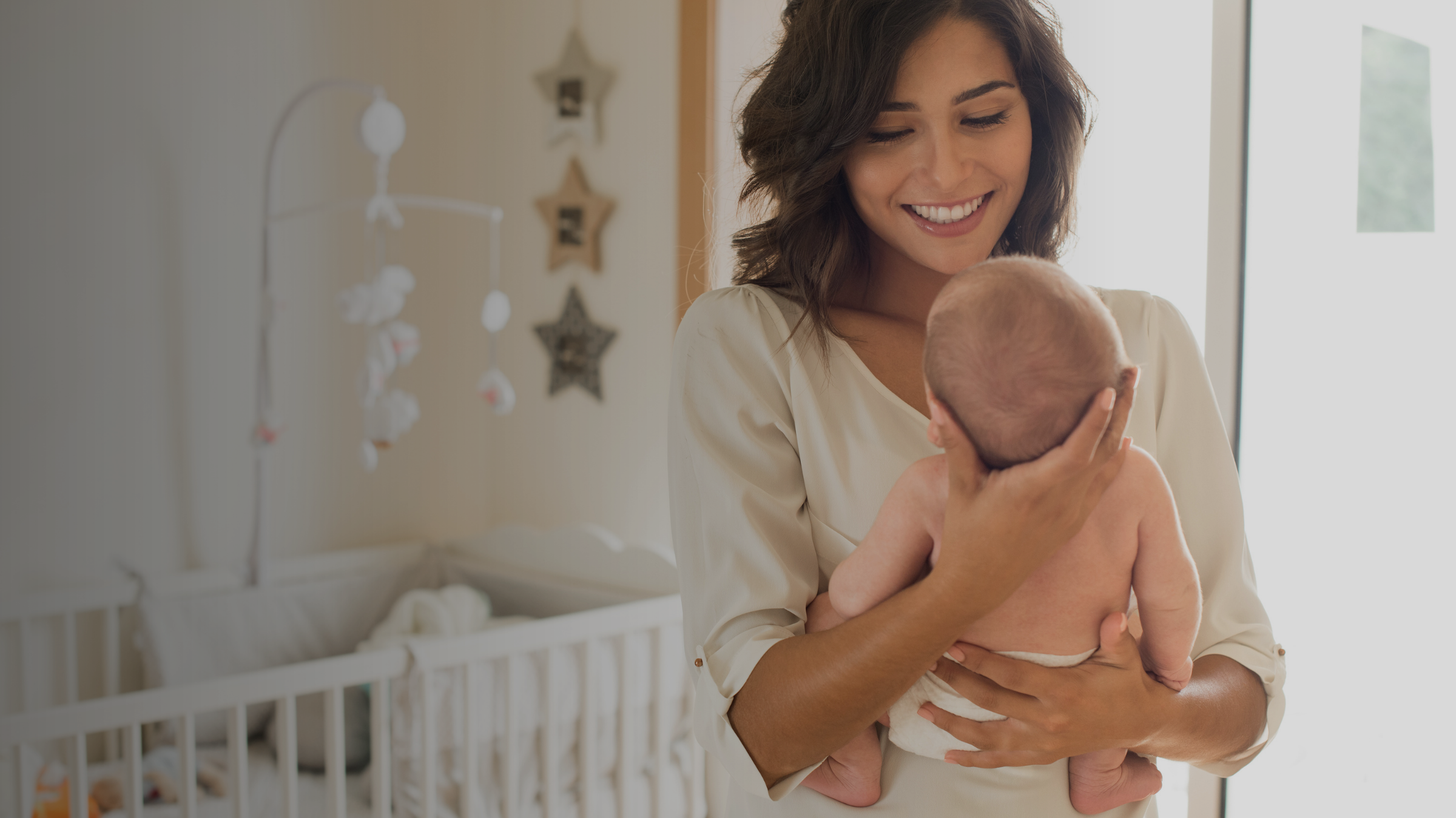 Woman holding a baby in a nursery with a crib and mobile in the background
