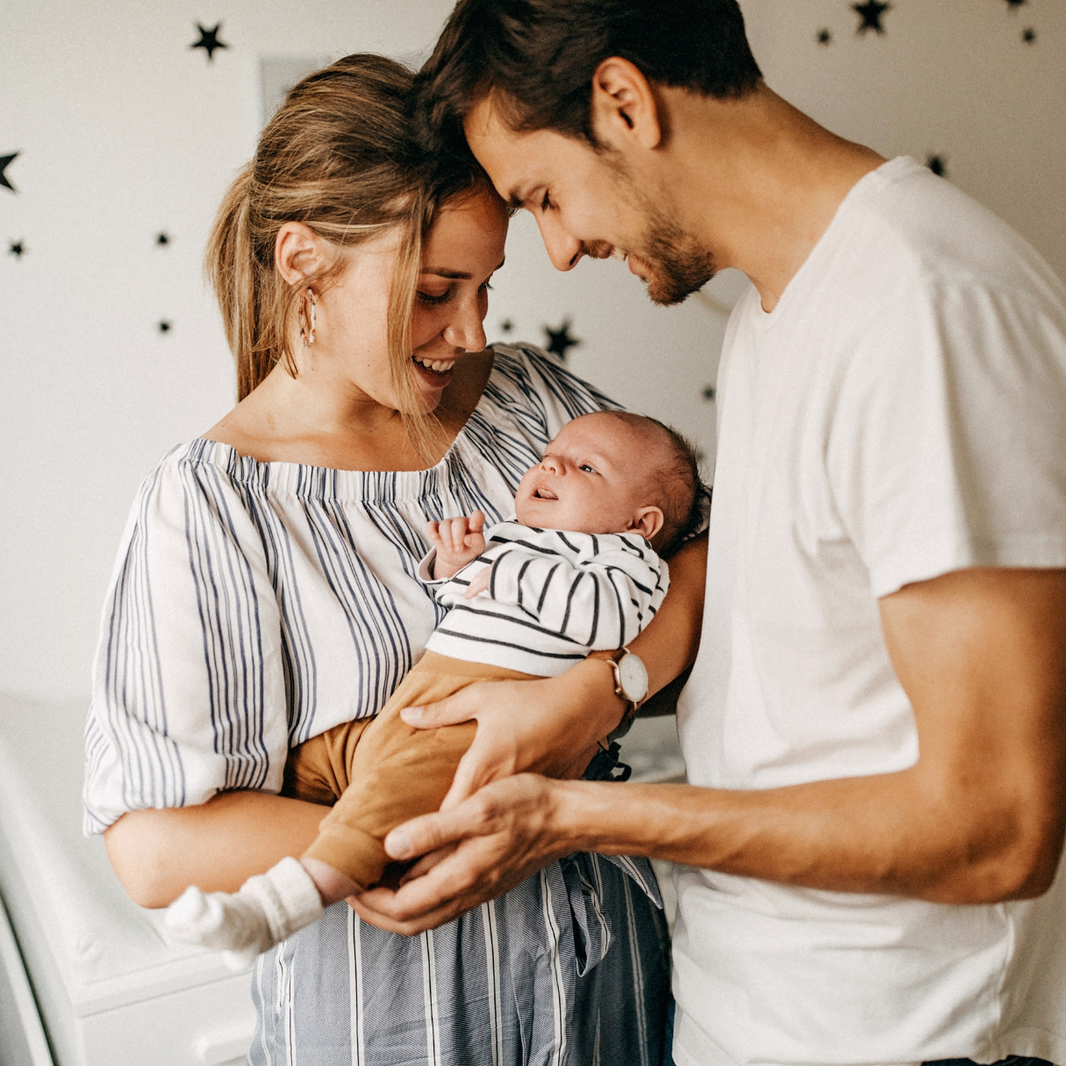 Family of three with a baby indoors against a star-patterned wall.